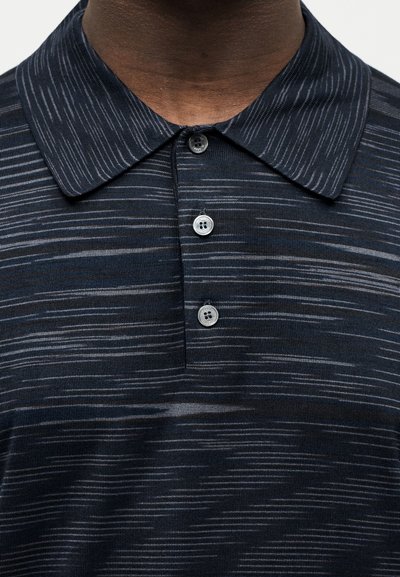 Κοντινό πλάνο σκούρου μπλε πόλο μπλουζάκι με ανοιχτές οριζόντιες ρίγες, τρία κουμπιά και μυτερό γιακά στο πάνω μέρος του στήθους και στο λαιμό ενός ατόμου.