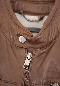 Braune Lederjacke mit hohem Kragen, silbernem Reißverschluss und Druckknopfverschluss. Verfügt über strukturiertes Leder und ein Kettendetail im Inneren.