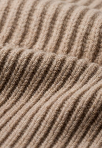 Tissu en tricot beige présentant une texture côtelée avec des lignes verticales marquées. Le fil doux et épais crée une apparence chaleureuse.