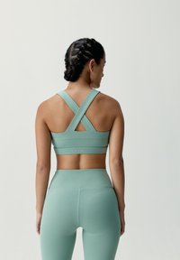 Mäta zelený športový podprsenka s prekríženými ramienkami, hladká textura a priliehavý strih. Zodpovedajúce legíny s vysokým pásom v rovnakých farbách.