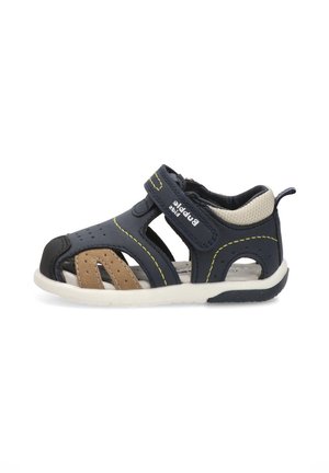 Sandalia para niño pequeño en azul marino y marrón, con puntera cerrada, correa ajustable de velcro, talón acolchado y suela blanca.