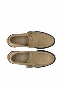 Paire de mocassins en daim beige avec semelles noires et larges brides maintenues par des boutons ronds en métal, vus de dessus sur fond blanc.