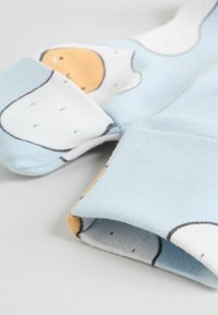 Blå bomullstyg med ett mönster av abstrakta stekta ägg. Manschetter i ljusbrun färg med tätt stickad struktur och kontrasterande innerfoder.