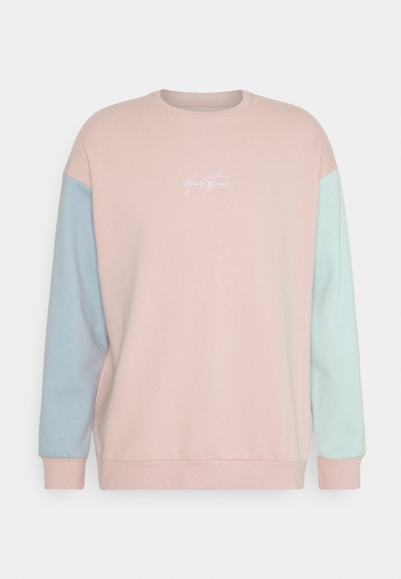 Sweat-shirt rose pastel avec manches bleu clair et vert menthe, col rond et logo blanc en cursive centré sur la poitrine.