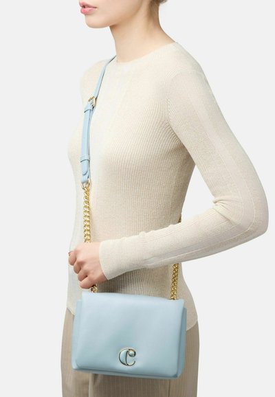 Gaiši zila ādas rokassomiņa ar gludu apdari, zelta ķēdes siksna un apaļš logotipa akcenti uz priekšpuses. Nēsāta kā crossbody stils.