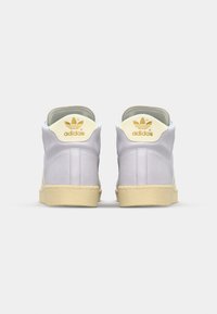 Ljust lila mocka sneakers i hög modell med beige gummisula och benvita detaljer. Guld "adidas"-logotyp på hälen och tungan.
