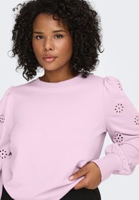 Light pink sweatshirt with puffed sleeves, floral cutouts on shoulders, and ribbed cuffs. Smooth fabric, casual design.