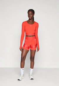 Piros, hosszú ujjú crop top és hozzá illő rövidnadrág, mindkettőn "NIKE PRO" logóval. Az anyag rugalmas, sportteljesítményre tervezve.