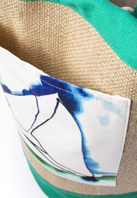 Nahaufnahme einer geflochtenen Strohtasche mit einem grünen Stoffoberkante und einer weißen Tasche mit blauen abstrakten Aquarellmustern.