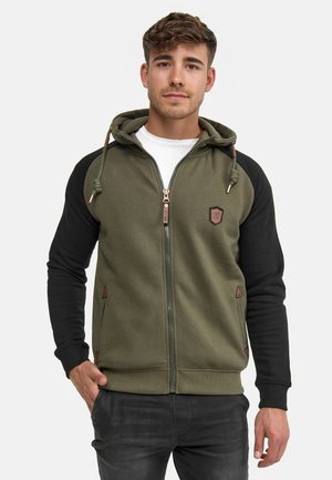 Sudadera verde oliva con mangas negras, cierre de cremallera en la parte delantera y capucha ajustable con cordón. Presenta parches y acentos inclinados. Textura suave.