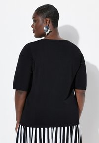 Top nero a maglia con maniche corte e scollo arrotondato. Indossato con una gonna a righe bianche e nere. Presenta un orlo a costine.
