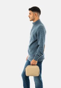 Ljusblå stickad tröja med hög krage, bruna läderdetaljer, tillsammans med en beige fyrkantig väska. Modellen står i profil.