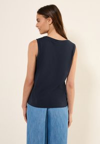 Top senza maniche di colore blu navy con scollatura tonda, realizzato in tessuto morbido; presenta una vestibilità comoda e un orlo dritto, abbinato a pantaloni in denim chiaro.