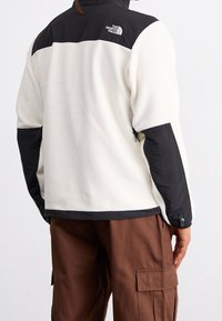 Fleecejacke in Creme mit schwarzen Nylonakzenten an Schultern und Ärmeln. Verfügt über verstellbare Bündchen und ein Logo am oberen Rücken.