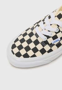 Crno-bež karirani platneni tenisice s bijelim vezicama i gumenim potplatom, s Vans logotipom na strani.