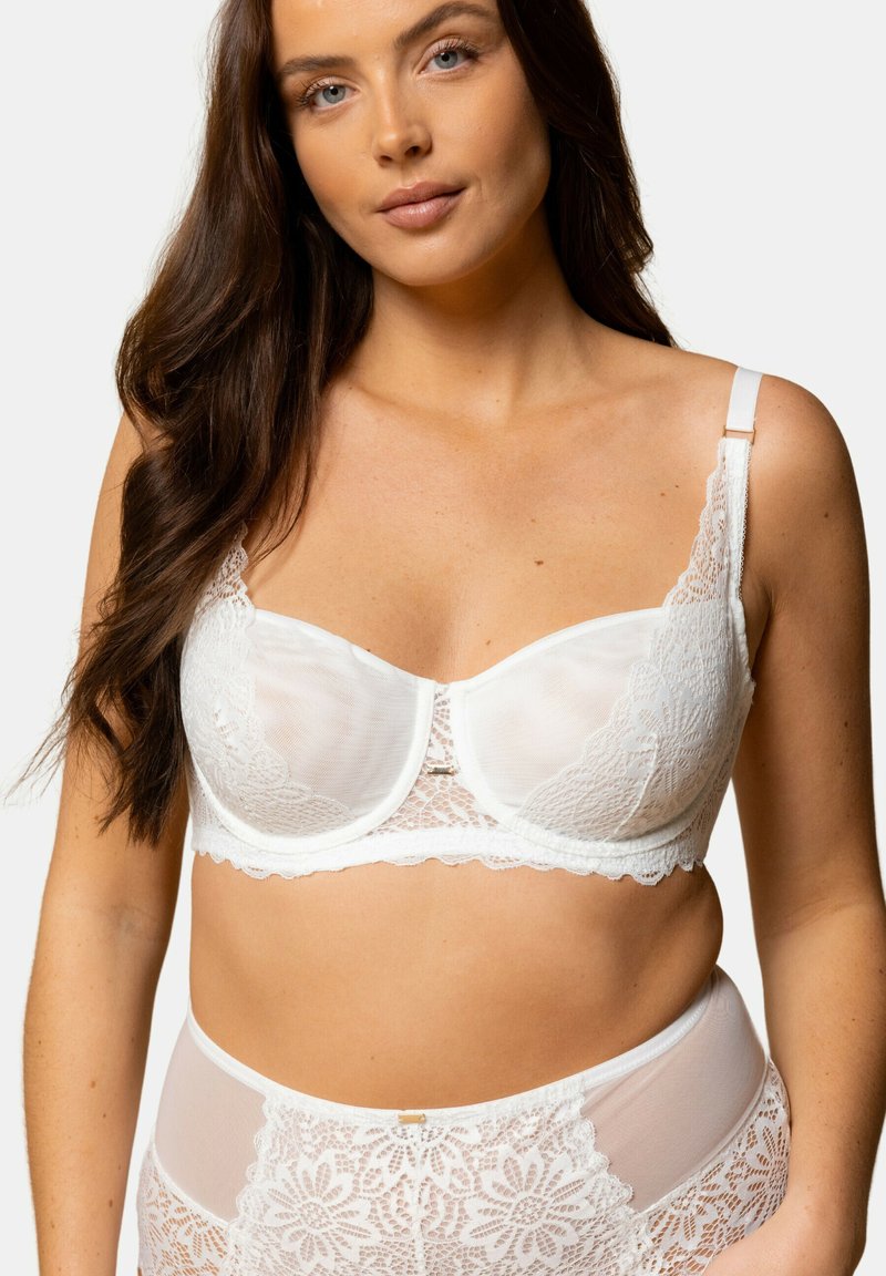 Soutien-gorge en dentelle blanche avec des panneaux en maille transparente, des détails en dentelle florale, un fermoir décoratif au centre et des bretelles réglables. Texture douce et délicate.
