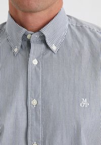 Striped button-up shirt in navy and white. Features a classic collar, front buttons, and a small embroidered logo on the left chest.