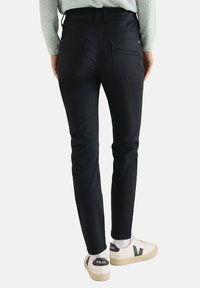 Sorte denim jeans med slim fit silhuet, der har to baglommer og en mid-rise talje, parret med hvide sneakers.
