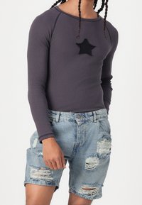 Långärmad grå ribbad topp med en svart stjärnpatch, i kombination med slitna ljusblå jeansshorts med fransade kanter och fastsatt midjeresår.