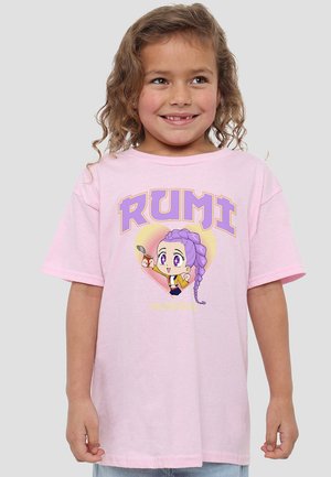 Smiling young girl with curly hair wearing a pink T-shirt featuring an anime character with purple braided hair and text "RUMI" and "HUNTRX."