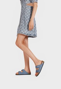 Sandali blu in suede con due fibbie regolabili, suola scura e dettaglio in sughero. Abbinati a un vestito di jeans a fantasia.