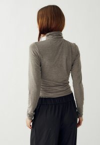 Pelēks garām piedurknēm turtlenecks tops ar pieguļošu dizainu un gludu tekstūru, apvienots ar melniem biksēm ar elastīgu jostasvietu. Skats tikai no aizmugures.