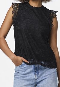 Top in pizzo nero con bordi scallopati, motivi floreali e maniche corte. Abbinato a jeans di denim a vita alta di colore blu chiaro.