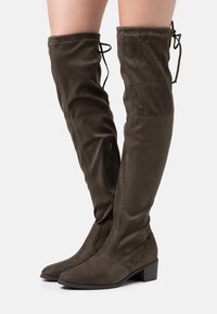 Botas hasta la rodilla de ante verde oliva con punta puntiaguda, tacón grueso y cordón ajustable en la parte superior, con un detalle de cremallera lateral.