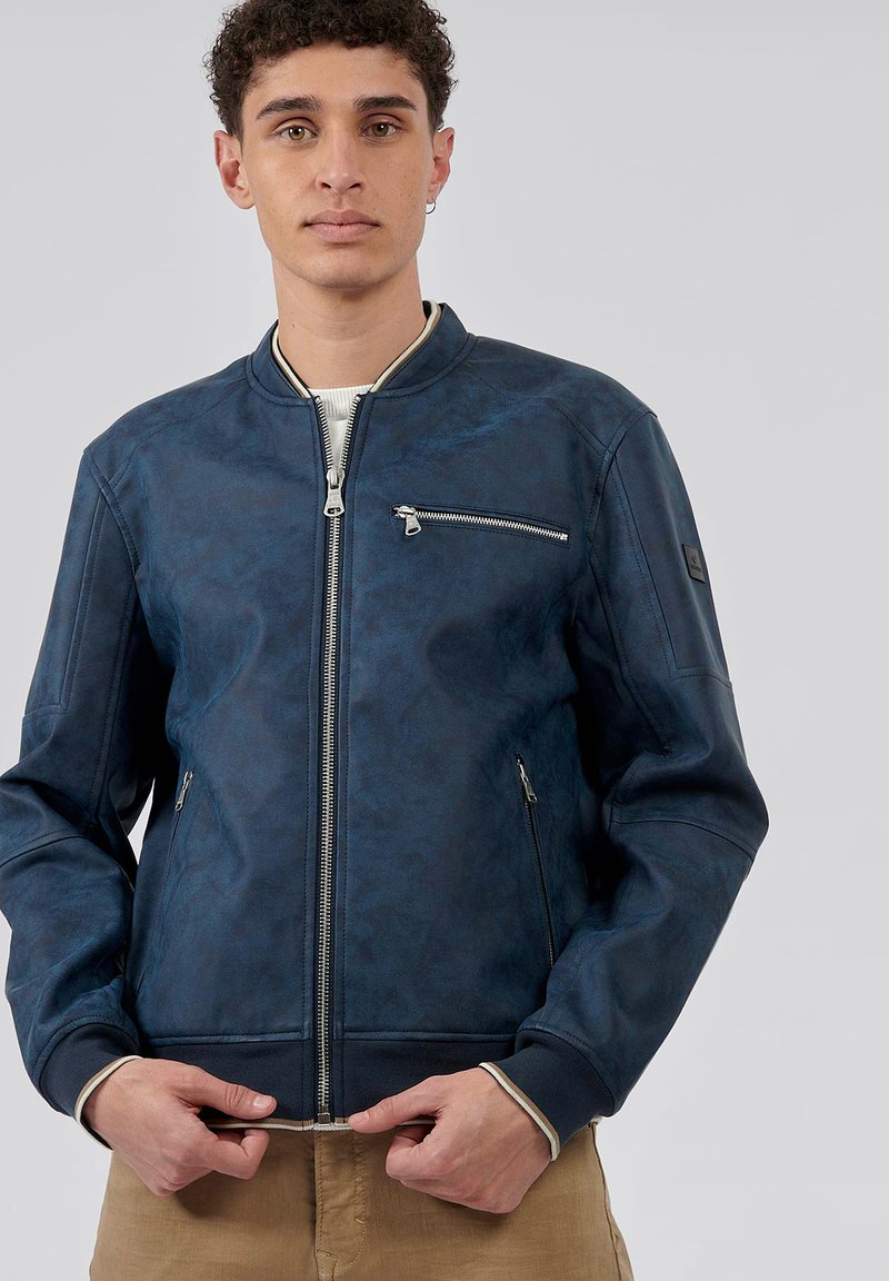 Veste bomber pour homme en simili cuir bleu marine. Dotée d'une fermeture éclair à l'avant, de poches latérales et d'une poche sur la poitrine avec des accents en métal argenté.