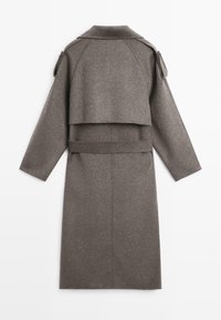 Lungo cappotto in lana marrone con design posteriore a strati, maniche lunghe e vita con cintura. Presenta un colletto pieghevole e una struttura minimalista.