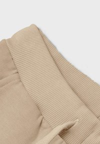Beige gerippter elastischer Bund mit Kordelzug an weichen Stoffhosen, Nahaufnahme, die Struktur und Nähte zeigt.