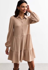 Light brown dress with a button-up front, collared neckline, and long sleeves. Features a tiered skirt with a textured fabric.