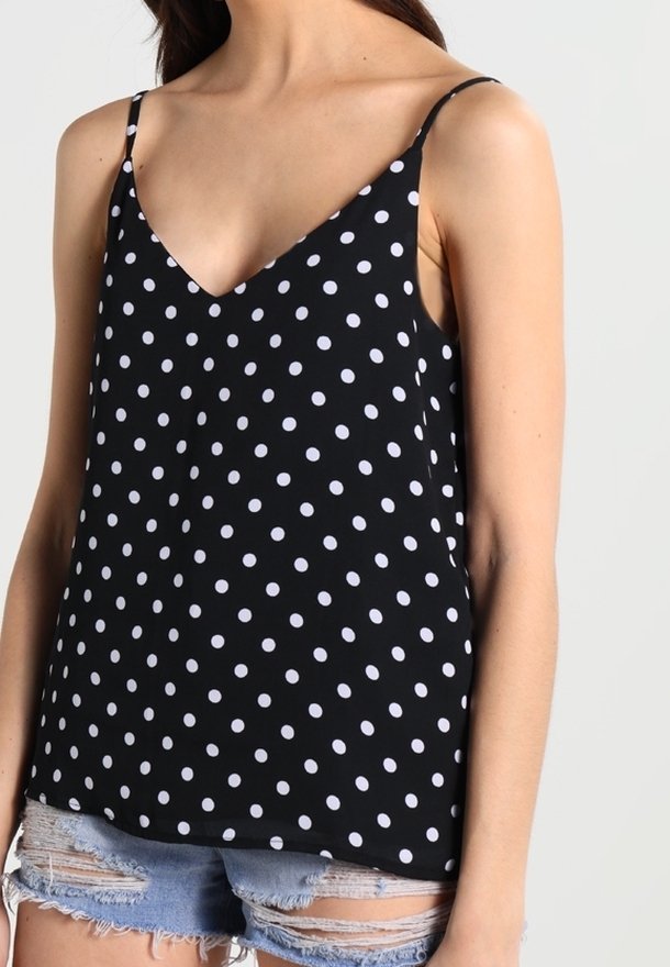 Svart ärmlös topp med v-ringning, prydd med vita prickar. Tillverkad av ett mjukt tyg, har den en avslappnad passform och tunna justerbara axelband.