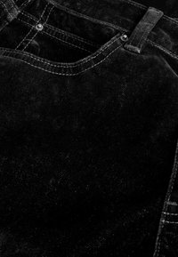 Zwarte spijkerbroek heeft een gestructureerd oppervlak met contrasterende witte stiksels. Bevat een voorzak en metalen knoopdetails op de tailleband.