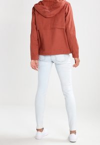 Rustfarvet jakke med hætte, med en cropped design. Sammen med lyseblå skinny jeans og hvide sneakers. Minimalistiske detaljer.