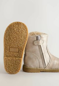 Metalliska guldankelboots med fuskpälsfoder, sidsibdragkedja och strukturerad gummisula. Har en platt klack och sömnadsdetaljer.
