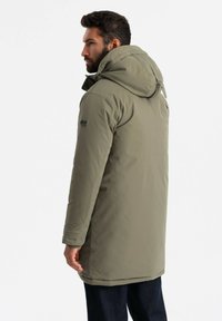 Olivgrüner Puffer-Mantel mit Kapuze, ausgestattet mit einem Reißverschluss, elastischen Bündchen und einem Logo-Patch am Ärmel. Glattes, isoliertes Material.