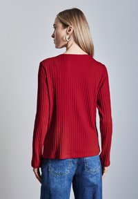 Rotes, geripptes Langarmshirt mit Rundhalsausschnitt, kombiniert mit lockeren Jeans aus Denim, die ein strukturiertes Design und eine lässige Passform zeigen.