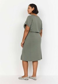 Rochie verde, cu maneci scurte, cu talie definită și slituri laterale. Textură netedă, material moale, până la genunchi. Purtați cu încălțăminte plată cu model floral.
