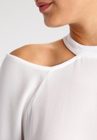 Vit off-shoulder topp med hög halsringning, med ett mjukt, lätt tyg och en slank utskärning nära kragen.