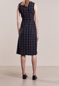 Marinblå ärmlös klänning med ett vitt rutmönster, skräddarsydd passform, knälång och med en dold dragkedja i ryggen. Lättviktsmaterial med mjuk textur.