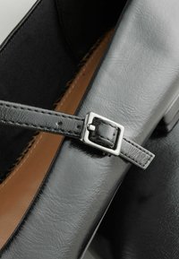 Černá kožená bota s texturovaným svrškem, elegantním páskem se stříbrnou sponou a světlou podšívkou.
