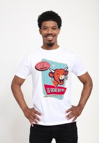 T-shirt bianco in cotone con una grafica colorata di mucca e il testo "La vache qui rit" in un design ispirato al vintage.