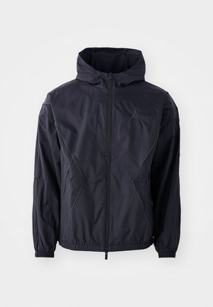 Schwarze Windjacke mit Kapuze, ausgestattet mit einem durchgehenden Reißverschluss, elastischen Bündchen und Seitentaschen. Strukturiertes Gewebe mit geometrischen Nähten.