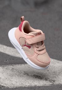 Růžová síťovaná teniska s bílou podrážkou, suchým zipem a akcentem s logem. Obuv má zaoblený tvar a měkkou texturu.
