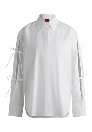 White button-up shirt with long sleeves, featuring ribbon ties on the sleeves and a curved hem. Made of smooth cotton fabric.