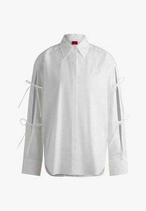Weißes Hemd mit langen Ärmeln und Knopfleiste, ausgestattet mit Bandbändern an den Ärmeln und einem abgerundeten Saum. Hergestellt aus glattem Baumwollstoff.