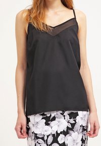 Top de camisolín negro de satén con escote en V transparente, tirantes finos y ajuste relajado, combinado con una falda blanca y negra con estampado floral.