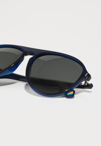 Ochelari de soare din plastic albastru cu lentile închise, având un accent curcubeu pe lateral și un design elegant și sportiv.