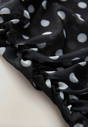 Black mesh fabric with white polka dots, featuring gathered texture and soft draping. Visible stitching detail accentuates the fabric’s flow.